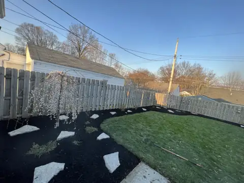 A curved mulched bed around a backyard lawn with established plants
