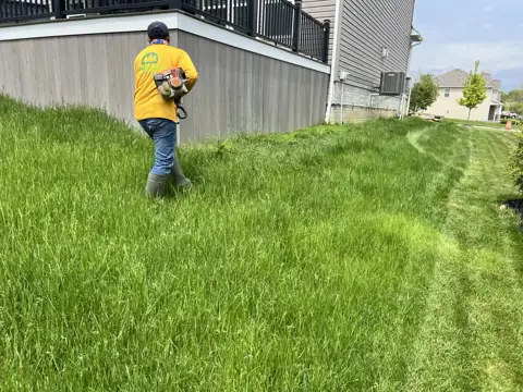A crew member trimming grass beside a building