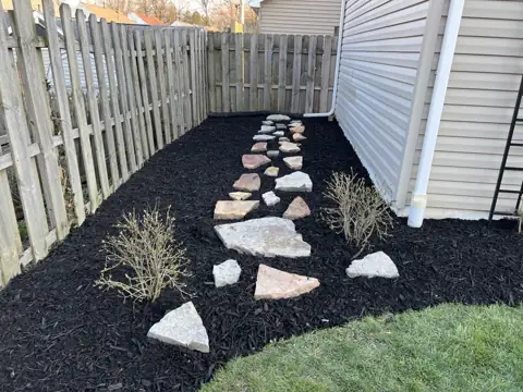 A dark mulched bed beside an existing stone path and fence