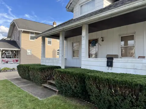 A trimmed hedge line beside porch steps and a sidewalk