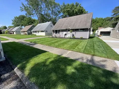 A sunny striped lawn and home under a blue sky